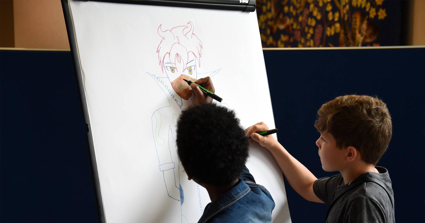 Deux jeunes dessinent un personnage de manga sur une grande feuille blanche