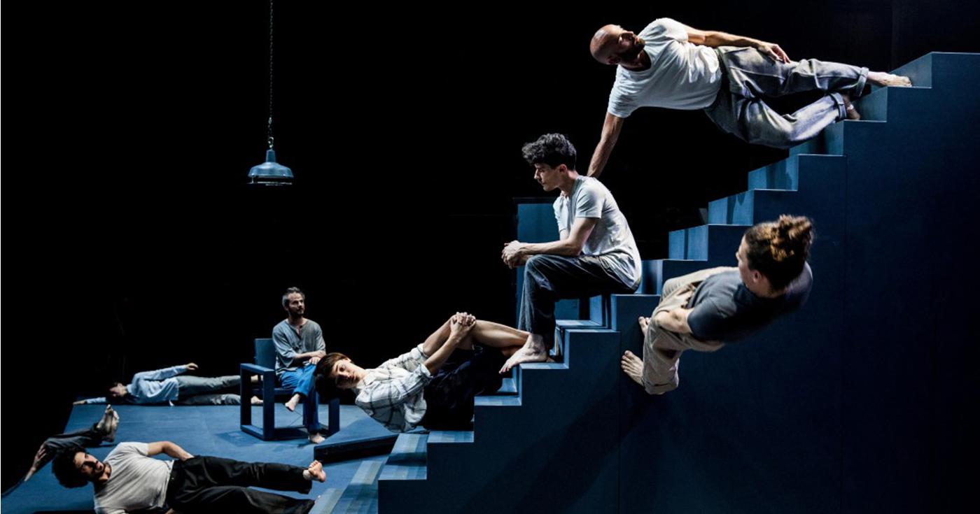 Phtotographie du spectacle Scala, des acteurs assis ou appuyés contre un escalier, jouant avec les lois de la gravité.