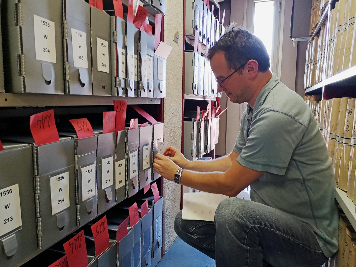Un homme place des étuiquettes sur des dossiesr dans un des magasins des Archives