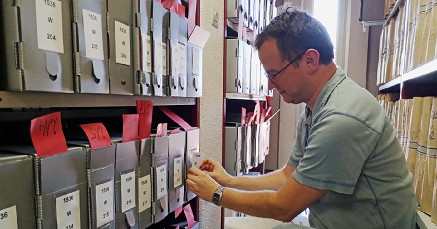 Un homme place des étuiquettes sur des dossiesr dans un des magasins des Archives