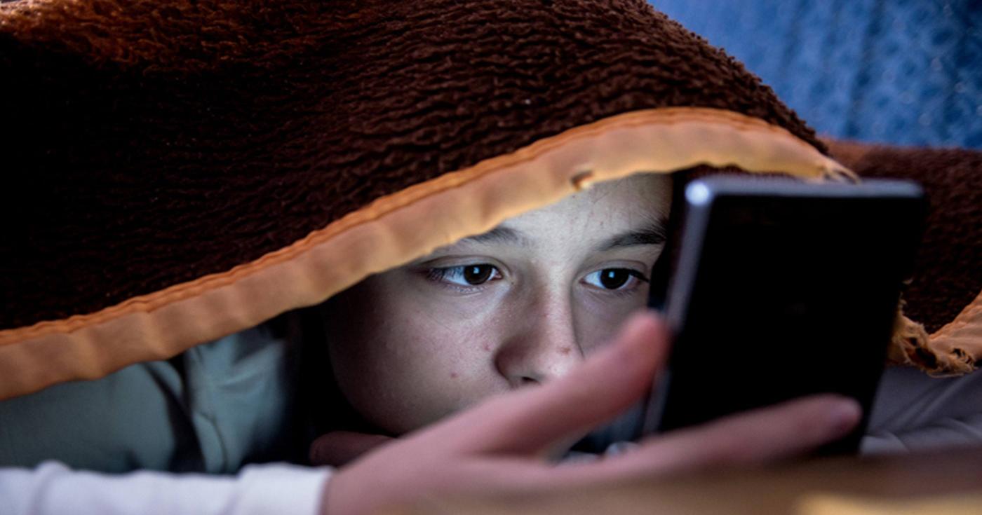 Campagne de sensibilisation aux écrans : la sécurité en questions - jeune sur son téléphone sous une couverture