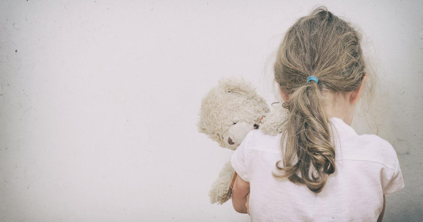 Enfant de dos serrant sa peluche contre elle