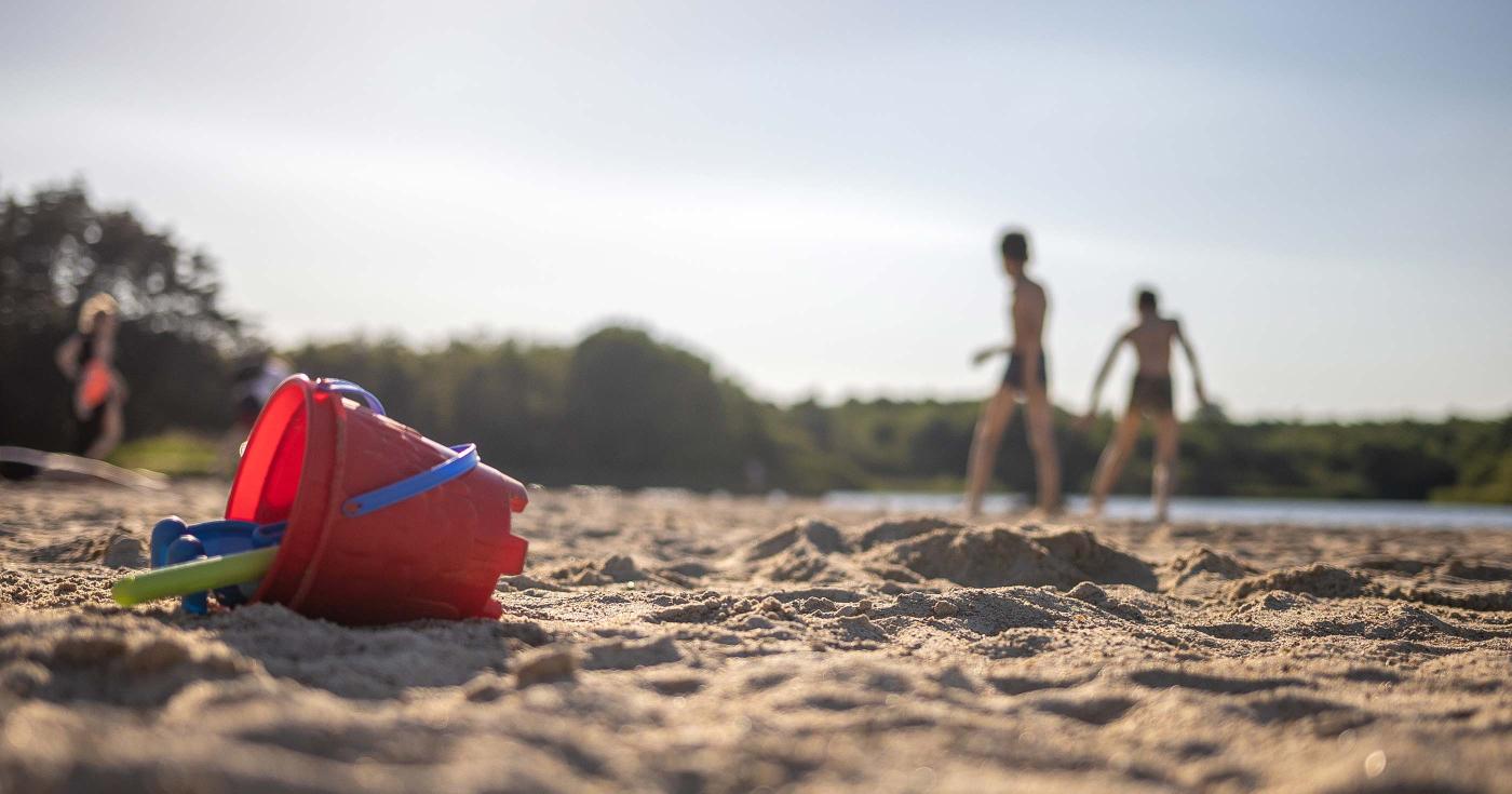 Alerte de niveau 2 à l’étang de la vallée - seau de plage au premier plan et enfant jouant dans le sable au second plan